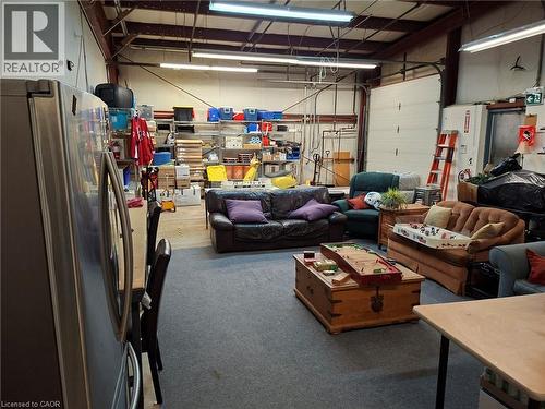 Spacious industrial interior featuring a roll-up garage door, exposed ceiling beams, fluorescent lighting, and a durable gray carpeted area - 920 Sheldon Court, Burlington, ON 