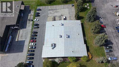 Aerial perspective of a commercial property featuring a large building with a light-colored roof, multiple parking areas, and mature landscaping - 920 Sheldon Court, Burlington, ON 