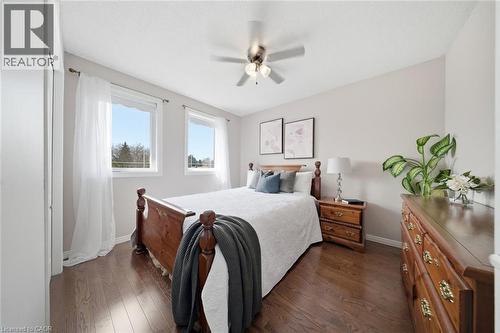 Bright room featuring wood-finish flooring, two windows with white trim, and a ceiling fan with integrated lighting - 200 Morrison Drive, Caledonia, ON - Indoor Photo Showing Bedroom