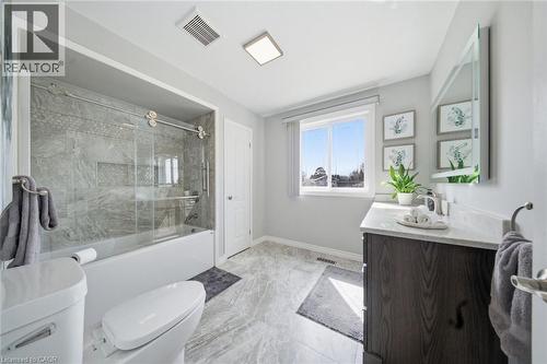 Bathroom featuring a white tub with clear glass sliding doors, gray tiled shower surround, a dark wood-finish vanity with a light countertop and undermount sink, and light gray tile flooring - 200 Morrison Drive, Caledonia, ON - Indoor Photo Showing Bathroom
