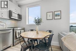 Compact kitchen area featuring stainless steel appliances, white cabinetry, hexagonal tile backsplash, and wood-finish flooring - 