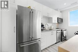 Modern kitchen featuring stainless steel appliances, white cabinetry, light-toned wood-finish flooring, a mosaic tile backsplash, and a window providing natural light - 