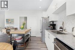 Kitchen featuring light wood-finish flooring, white cabinetry, integrated stainless steel appliances, a stainless steel sink with a gooseneck faucet, and a mobile island with a butcher block counterto - 