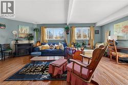 Living area featuring hardwood flooring, light blue wall paint, exposed ceiling beams, a built-in fireplace with a hearth, and dual windows - 