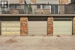 Three individual garage spaces featuring panel-style doors, brick columns, and a concrete driveway - 