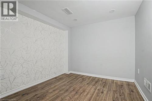 Accent wall featuring a subtle branch pattern, wood-finish flooring, recessed lighting, white baseboards, and neutral wall paint - 60 Postmaster Drive, Kitchener, ON - Indoor Photo Showing Other Room