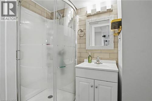 Compact bathroom featuring a curved glass shower enclosure with frosted accents, a white vanity with an integrated sink, a framed mirror, and a wall-mounted light fixture - 60 Postmaster Drive, Kitchener, ON - Indoor Photo Showing Bathroom