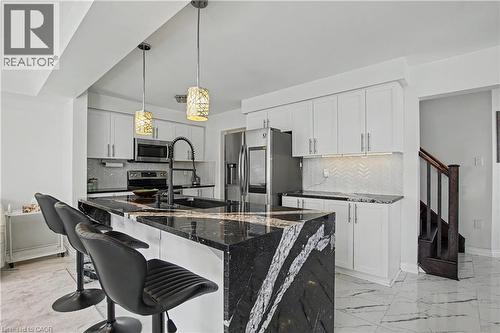 Kitchen featuring a large waterfall island with a polished stone surface, white cabinetry, stainless steel appliances, and a herringbone mosaic tile backsplash - 60 Postmaster Drive, Kitchener, ON - Indoor Photo Showing Kitchen With Upgraded Kitchen