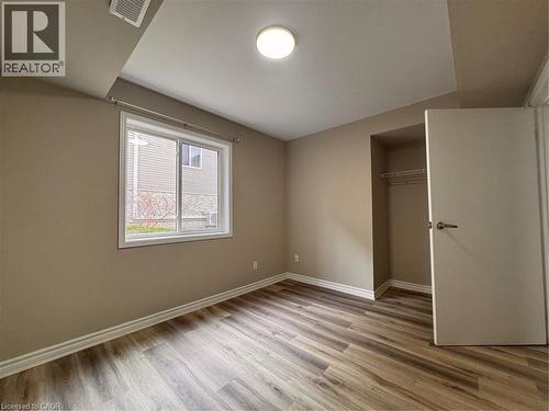 Spacious room featuring wood-finish flooring, neutral-toned walls, a large window, a built-in closet with wire shelving, and a flush-mount ceiling light fixture - 44 Walnut Street Unit# E01, Kitchener, ON - Indoor Photo Showing Other Room