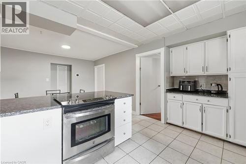 Kitchen featuring a built-in stainless steel range, dark stone countertops, white cabinetry, and white tile flooring - 2934 Baker Road, Niagara Falls, ON - Indoor Photo Showing Kitchen