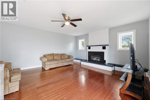 Spacious living area featuring wood-finish flooring, a white brick fireplace with a dark-tiled hearth and surround, and two windows providing natural light - 2934 Baker Road, Niagara Falls, ON - Indoor Photo Showing Living Room With Fireplace