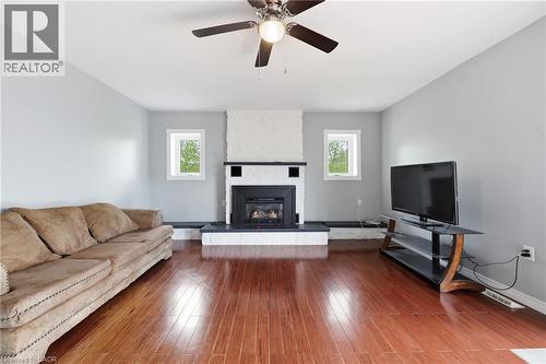 Living room featuring wood-finish flooring, a white brick fireplace surround, an integrated black fireplace insert, and two transom windows - 2934 Baker Road, Niagara Falls, ON - Indoor Photo Showing Living Room With Fireplace