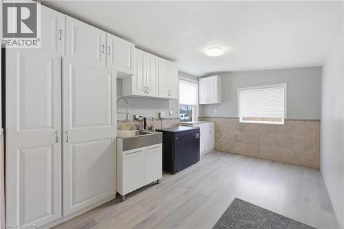 Efficient utility space featuring extensive white cabinetry, a stainless steel utility sink with a high-arc faucet, light wood-finish flooring, and a tiled half-wall - 2934 Baker Road, Niagara Falls, ON - Indoor Photo Showing Kitchen With Double Sink
