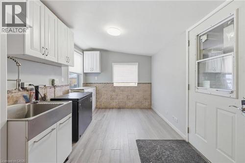 Kitchen area featuring white upper and lower cabinetry, a stainless steel farmhouse sink with a gooseneck faucet, light wood-finish flooring, and a tiled accent wall - 2934 Baker Road, Niagara Falls, ON - Indoor Photo Showing Kitchen