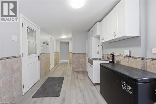 Functional utility space featuring light wood-finish flooring, white cabinetry, a stainless steel sink with a gooseneck faucet, and wainscoting with a mosaic tile border - 2934 Baker Road, Niagara Falls, ON - Indoor Photo Showing Other Room