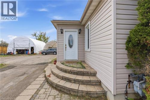 Property exterior featuring neutral-toned siding, a white entry door with an oval glass insert, and decorative exterior lighting fixtures - 2934 Baker Road, Niagara Falls, ON - Outdoor With Exterior