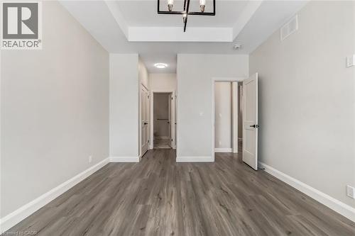 Photos from a similar model for illustration purposes only. Spacious room with wood-finish flooring, crisp white baseboards, and a tray ceiling featuring a contemporary chandelier - 7 Boer Drive, Simcoe, ON - Indoor Photo Showing Other Room