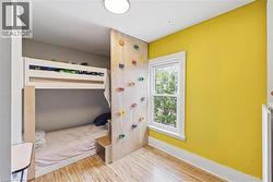Room featuring wood-finish flooring, a bright yellow accent wall, and a built-in bunk bed structure with an integrated climbing wall - 