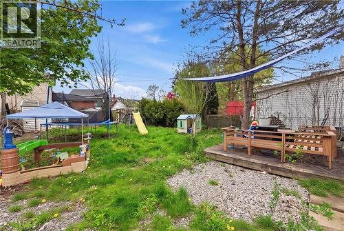 Expansive backyard featuring a wood deck with built-in bench seating, mature trees, and a gravel patio area - 54 Evan Street, Welland, ON - Outdoor