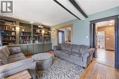 Living area featuring built-in shelving with cabinetry, exposed ceiling beams, wood-finish flooring, and a decorative archway - 54 Evan Street, Welland, ON - Indoor Photo Showing Living Room