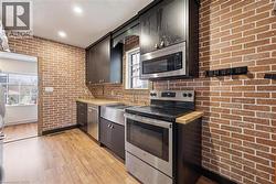Kitchen featuring exposed brick walls, wood-finish flooring, dark wood cabinetry, a stainless steel farm sink, and stainless steel appliances - 