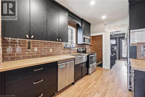 Kitchen featuring black cabinetry, butcher block countertops, exposed brick backsplash, stainless steel appliances, and wood-finish flooring - 54 Evan Street, Welland, ON - Indoor Photo Showing Kitchen
