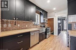 Kitchen featuring black cabinetry, butcher block countertops, exposed brick backsplash, stainless steel appliances, and wood-finish flooring - 