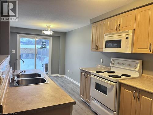 Kitchen featuring wood-finish cabinetry, a double basin stainless steel sink with a gooseneck faucet, an electric range, an over-the-range microwave, and light-toned countertops - 193 Prosperity Drive, Kitchener, ON - Indoor Photo Showing Kitchen With Double Sink