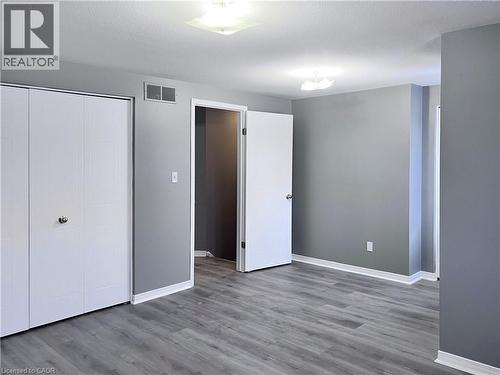 Interior room featuring wood-finish flooring, light grey walls, white baseboards, and two overhead flush-mount light fixtures - 193 Prosperity Drive, Kitchener, ON - Indoor Photo Showing Other Room