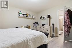 Spacious room featuring light-toned walls, wood-finish flooring, a wall-mounted shelf, and an interior door opening to an additional area - 