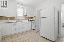 Kitchen featuring white cabinetry with silver-tone hardware, a stainless steel sink, beige tiled backsplash, and light-toned tile flooring - 