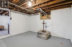 Unfinished basement space featuring exposed wooden ceiling joists, concrete block walls, painted concrete flooring, and visible plumbing and electrical lines - 