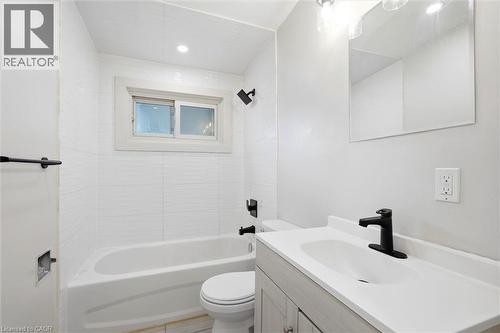 Bathroom featuring a white bathtub with subway tile surround, matte black shower fixtures, a single-pane window, a vanity with a white countertop and integrated sink, and a matte black faucet - 16 Ronaldshay Avenue, Hamilton, ON - Indoor Photo Showing Bathroom