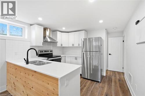 Modern kitchen featuring white shaker cabinetry, stainless steel appliances, a wood-finish island with a double sink, white quartz countertops, and wood-finish flooring - 16 Ronaldshay Avenue, Hamilton, ON - Indoor Photo Showing Kitchen With Double Sink With Upgraded Kitchen
