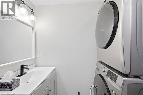 Laundry area featuring a stacked washer and dryer, adjacent to a vanity with an undermount sink, a matte black faucet, and a wall-mounted mirror - 16 Ronaldshay Avenue, Hamilton, ON - Indoor Photo Showing Laundry Room
