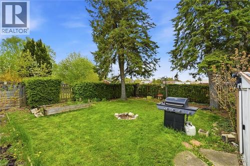 Expansive backyard with a manicured lawn, established trees, and a stone fire pit - 16 Ronaldshay Avenue, Hamilton, ON - Outdoor