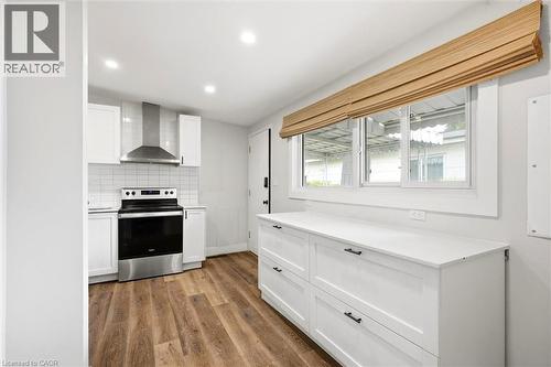 Modern kitchen featuring white shaker cabinetry, stainless steel range with matching hood, white subway tile backsplash, wood-finish flooring, and a window with a woven wood shade - 16 Ronaldshay Avenue, Hamilton, ON - Indoor
