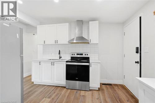 Modern kitchen featuring white shaker-style cabinetry, a subway tile backsplash, and wood-finish flooring - 16 Ronaldshay Avenue, Hamilton, ON - Indoor Photo Showing Kitchen