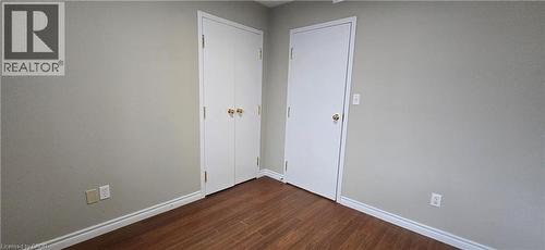 Interior space featuring wood-finish flooring, light-toned walls, white baseboards, and two white doors with brass-toned hardware - 274 E Highland Road E Unit# 10, Kitchener, ON - Indoor Photo Showing Other Room