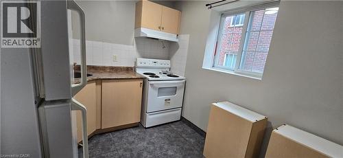 Compact kitchen featuring a white electric range, white ceramic tile backsplash, upper and lower cabinetry, a refrigerator, and dark tile flooring - 274 E Highland Road E Unit# 10, Kitchener, ON - Indoor Photo Showing Kitchen