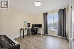 Spacious room featuring wood-finish flooring, light-colored walls, a large window with white trim, and a modern ceiling light fixture - 