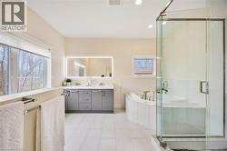 Spacious bathroom featuring a glass-enclosed shower, corner soaking tub, and a double vanity with an illuminated mirror - 