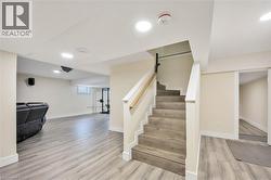 Finished lower level featuring wood-finish flooring, recessed lighting, a white painted staircase with wood handrail, and a window - 