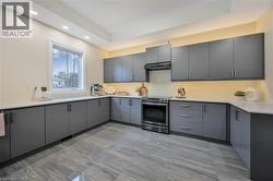 Contemporary kitchen featuring extensive gray cabinetry, light countertops, stainless steel range and hood, under-cabinet lighting, and large format tiled flooring - 