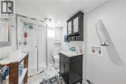 Compact bathroom featuring a corner shower enclosure with a curved glass door, a dark wood-finish vanity with a light-colored countertop, and a wall-mounted medicine cabinet - 235 Larch Street, Hamilton, ON - Indoor Photo Showing Bathroom