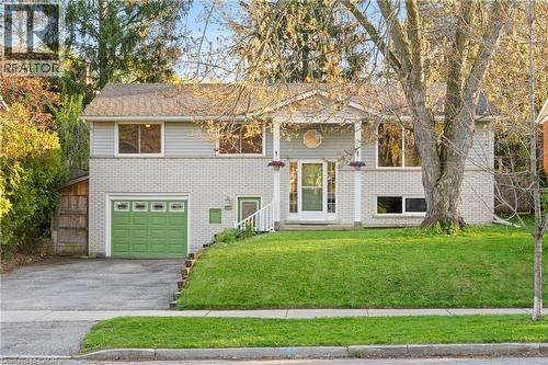 Split-level residence featuring a light gray brick and siding exterior, a prominent green garage door, a front porch with white columns, and a landscaped front lawn - 183 Harvard Road, Waterloo, ON - Outdoor