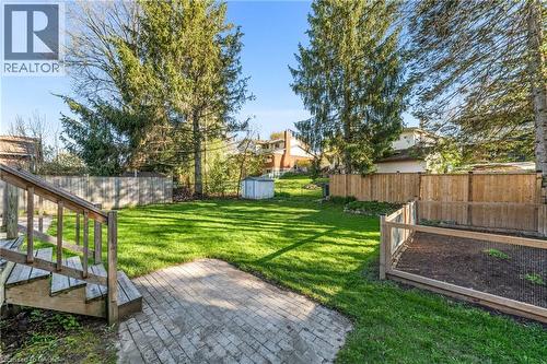 Expansive backyard featuring a lush lawn, mature evergreen trees, a paver patio, a wood deck with stairs, and wood privacy fencing - 183 Harvard Road, Waterloo, ON - Outdoor With Backyard