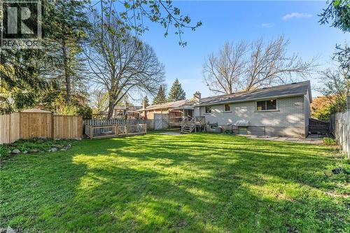 Expansive backyard featuring a lush lawn, privacy fencing, mature trees, and a brick exterior dwelling with a wood deck and patio space - 183 Harvard Road, Waterloo, ON - Outdoor