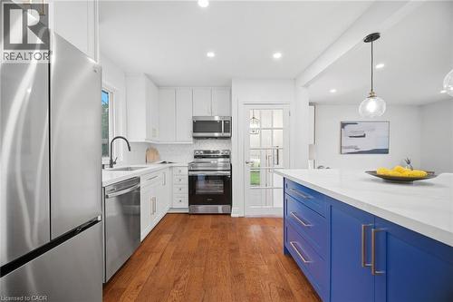 Contemporary kitchen featuring white cabinetry, stainless steel appliances, a contrasting blue island with a white countertop, and hardwood flooring - 1376 Royal Drive, Burlington, ON - Indoor Photo Showing Kitchen With Upgraded Kitchen