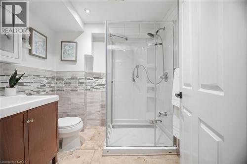 Glass-enclosed shower with multiple spray fixtures, wood-finish vanity with white rectangular sink, white toilet, and neutral-toned floor tiling - 1376 Royal Drive, Burlington, ON - Indoor Photo Showing Bathroom